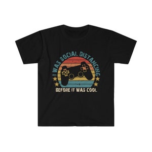 May include: Black t-shirt with a retro-style graphic of a video game controller and the text "I was social distancing before it was cool."