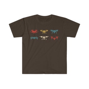 May include: A brown t-shirt featuring a retro design of six drones in various colors: red, yellow, teal, blue, white, and red. The drones are arranged in two rows of three. The shirt is made of a soft material.