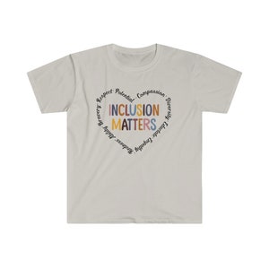 May include: A light gray t-shirt with a circular design featuring the words "Inclusion Matters" in colorful letters surrounded by a circle of words including "Respect, Potential, Compassion, Diversity, Empathy, Gratitude, Kindness, Bravery,  Adult,  Happiness".