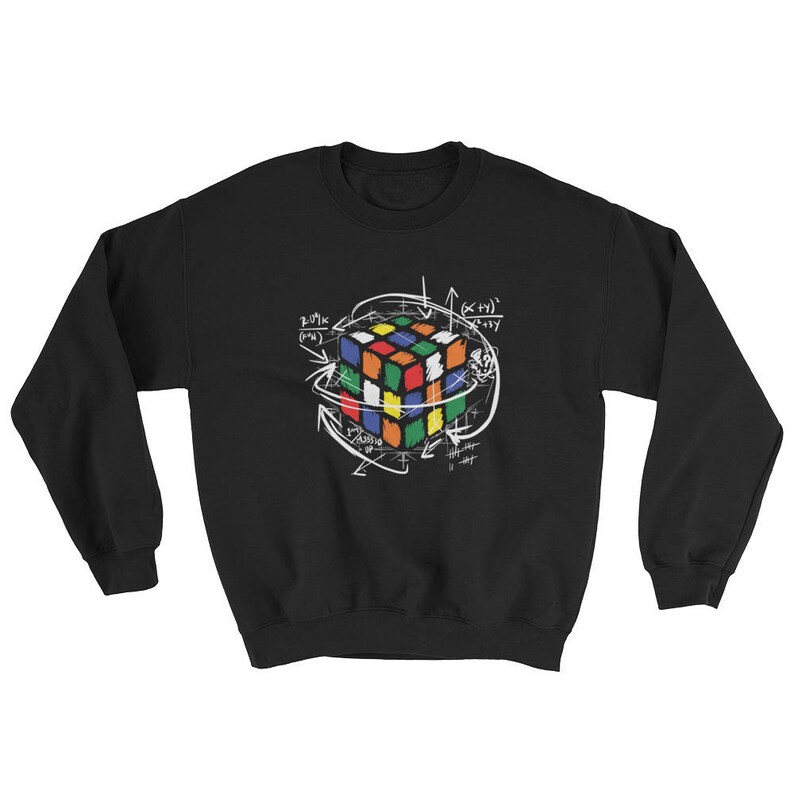 Puede incluir: Sudadera negra con un dise&ntilde;o de cubo de Rubik colorido, rodeado de flechas blancas y ecuaciones matem&aacute;ticas. El cubo tiene cuadrados rojos, naranjas, amarillos, verdes, azules y blancos. El dise&ntilde;o est&aacute; centrado en el pecho.