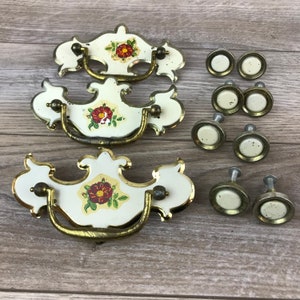 May include: Three ornate white and gold cabinet pulls with floral designs and eight round white and gold knobs.
