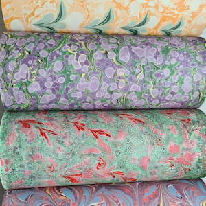 May include: Four rolls of decorative paper with unique marbled patterns. The top roll features orange and white swirls with green leaf-like accents. Below are rolls in purple, green, pink, and blue, each with distinct, colorful designs.