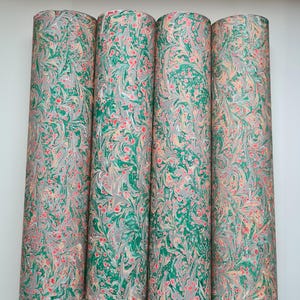 May include: Four rolls of decorative paper with a marbled design. The paper features a pattern of green, grey, red, and peach swirls and dots. The rolls are cylindrical and stand upright against a white background.