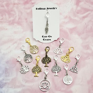 May include: A set of 10 silver and gold charm clips featuring various designs, including trees, lotuses, and a Celtic knot. The charms are attached to silver lobster clasps. The charms are displayed on a pink background with a white card that reads "Kelissa Jewelry Clip-On Charm".