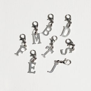 May include: Silver letter charms with a lobster clasp. The letters are F, M, B, D, T, S, E, and J.