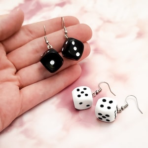 May include: A pair of earrings featuring black and white dice charms. The black dice have white dots and the white dice have black dots.