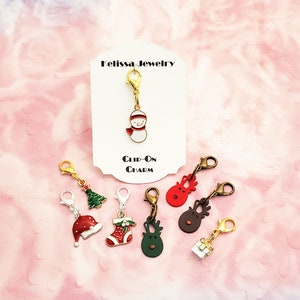 May include: Set of 7 gold-tone Christmas themed clip-on charms. Charms include a snowman, a Christmas tree, a stocking, a Santa hat, a reindeer, a reindeer head, and a gift box. The charms are on a white background with the text "Melissa Jewelry" and "Clip-On Charm".