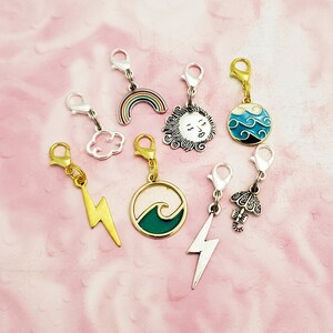 May include: A set of eight charm zipper pulls featuring various designs, including a rainbow, a sun, a cloud, a wave, a lightning bolt, and an umbrella. The charms are made of metal and have a silver or gold finish.
