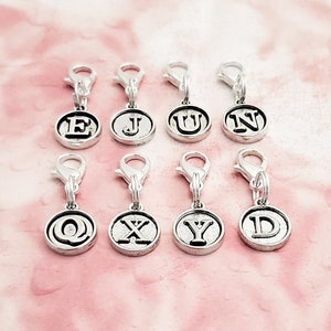 May include: Eight silver charms with letter initials E, J, U, N, Q, X, Y, and D. The charms are attached to silver lobster clasps.
