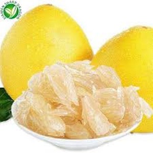 Pode incluir: Close-up de dois pomelos amarelos grandes e uma tigela branca cheia de segmentos descascados. Os pomelos t&ecirc;m pele lisa. Uma folha verde &eacute; vis&iacute;vel.