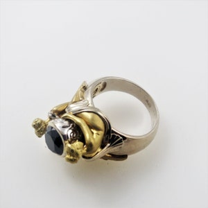 May include: A silver and gold ring with a black gemstone set in a detailed floral design.