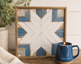 Puede incluir: Una pieza de arte mural cuadrada de madera con un patrón de estrella geométrico hecho de listones de madera blanca, azul y natural desgastados. La obra está enmarcada en un borde de madera de tono medio y muestra un acabado rústico.