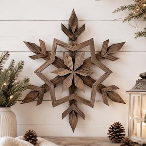 Puede incluir: Una gran decoración de pared con forma de copo de nieve de seis puntas, construida con listones de madera marrón desgastada. El diseño presenta un patrón de estrella central con brazos geométricos angulares y textura de veta natural.