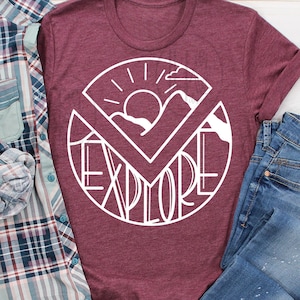 May include: A maroon t-shirt with a white graphic design of a sun, mountains, and the word "explore" in a circle.