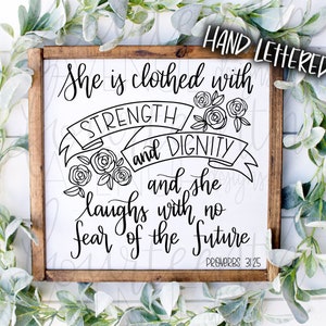 May include: A wooden sign with a white background and black lettering. The sign reads "She is clothed with STRENGTH and DIGNITY and she laughs with no fear of the future" and "PROVERBS 31:25".
