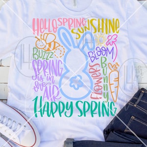 May include: White t-shirt with a colorful graphic design featuring a bunny, flowers, a bee, a carrot, and the text "Hello Spring Sunshine, Buzz, Spring is in the Air, Happy Spring, Bloom, Bunny, Flowers".