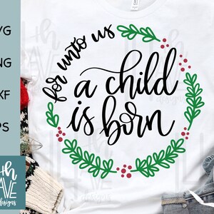 May include: White t-shirt with a green and red wreath design and the text "For unto us a child is born".