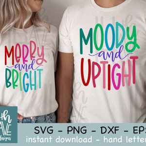 Könnte beinhalten: Zwei weiße T-Shirts mit buntem handgeschriebenen Text. Das erste Shirt sagt "Merry and Bright" in Regenbogenfarben. Das zweite Shirt sagt "Moody and Uptight" in Regenbogenfarben.