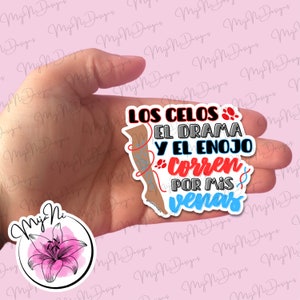 May include: A sticker with the text "LOS CELOS EL DRAMA Y EL ENOJO CORREN POR MIS VENAS" in black, red, and blue. The sticker also features a graphic of a leg with a patterned stocking. A second sticker with a pink flower is also visible.