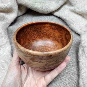 May include: A small, wooden bowl with a brown and orange marbled pattern. The bowl is hand-turned and has a smooth, polished finish.