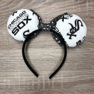 May include: Black headband with white fabric mouse ears featuring the Chicago White Sox logo. The ears are decorated with black glitter.