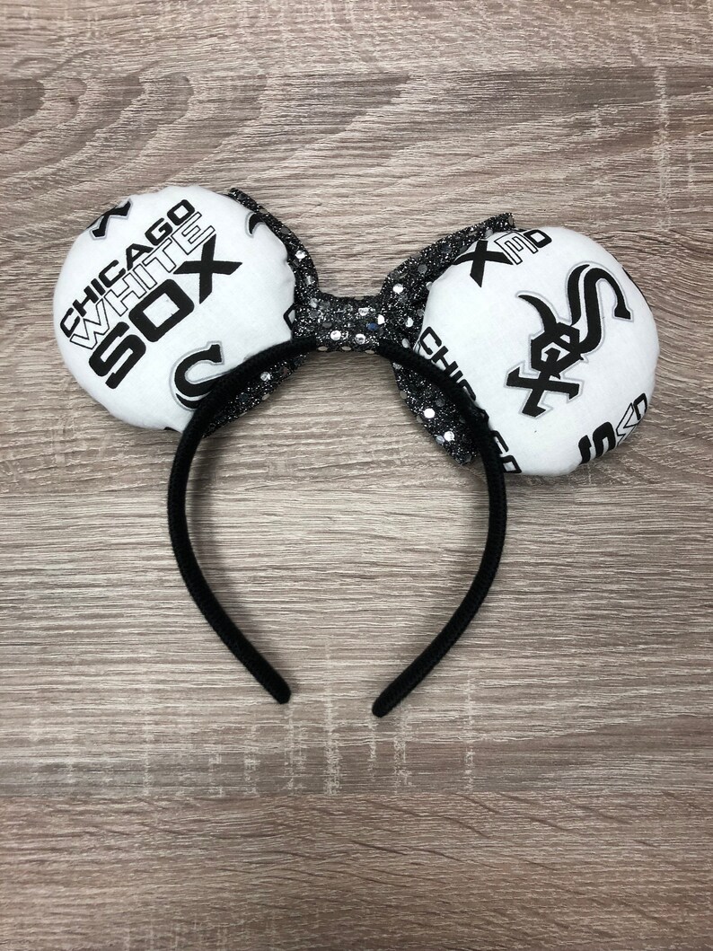May include: Black headband with white fabric mouse ears featuring the Chicago White Sox logo. The ears are decorated with black glitter.