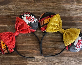 Könnte beinhalten: Ein Paar schwarze Kopfband-Mäuseohren mit roten und goldenen Paillettenbögen. Die Ohren sind mit einem Logo der Kansas City Chiefs und anderen Teamgrafiken verziert.