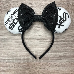 May include: White and black baseball-themed headband with a black bow and a white headband. The headband features the text "Chicago White Sox" on one side and the Chicago White Sox logo on the other side.