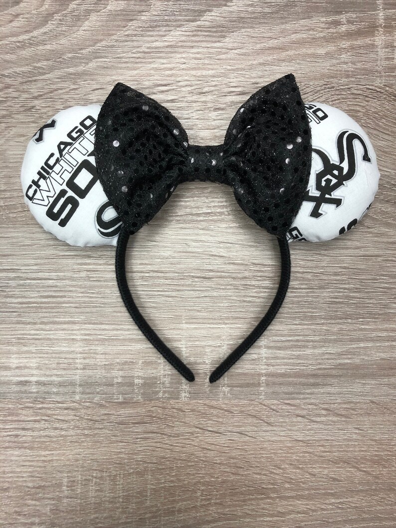 May include: White and black baseball-themed headband with a black bow and a white headband. The headband features the text "Chicago White Sox" on one side and the Chicago White Sox logo on the other side.