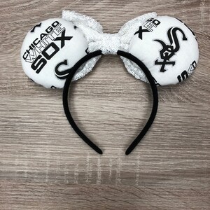 May include: White and black fabric headband with a bow and two large fabric ears. The ears are decorated with the Chicago White Sox logo and text.