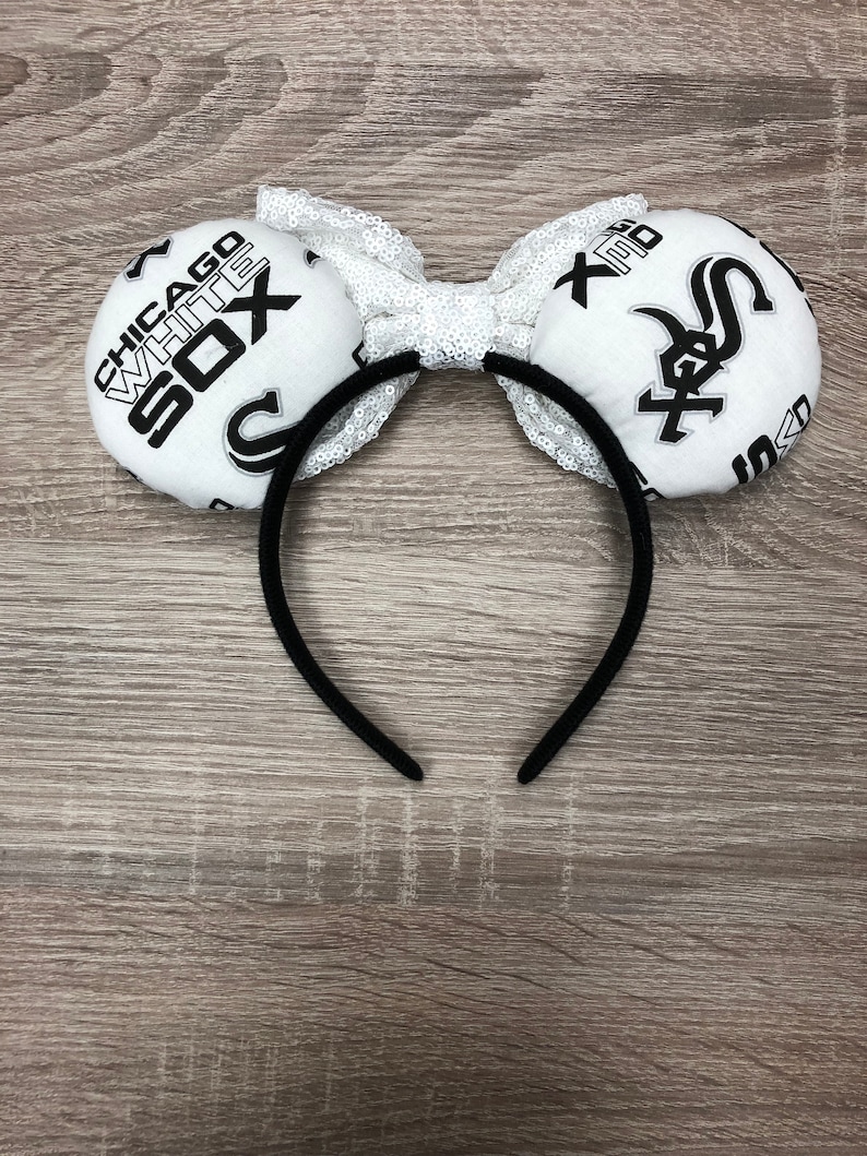 May include: White and black fabric headband with a bow and two large fabric ears. The ears are decorated with the Chicago White Sox logo and text.