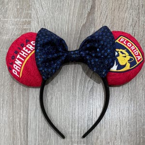 Könnte beinhalten: Rote und blaue Mäuseohren mit einem schwarzen Stirnband. Die Ohren sind mit den Worten "Florida Panthers" bestickt.