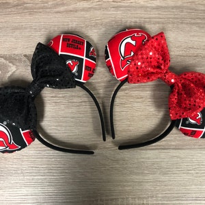 May include: A pair of black headband mouse ears with red and black fabric covered ears featuring the New Jersey Devils logo and a red and black glitter bow.