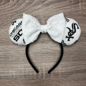 May include: White and black fabric headband with a white sequin bow and two fabric circles with the text "Chicago White Sox" and a baseball logo.
