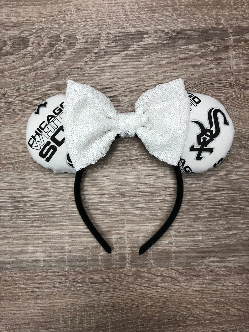 May include: White and black fabric headband with a white sequin bow and two fabric circles with the text "Chicago White Sox" and a baseball logo.