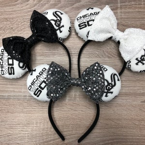 May include: A pair of black and white mouse ears with a black and white bow. The ears are decorated with the words "Chicago White Sox" and the team logo.