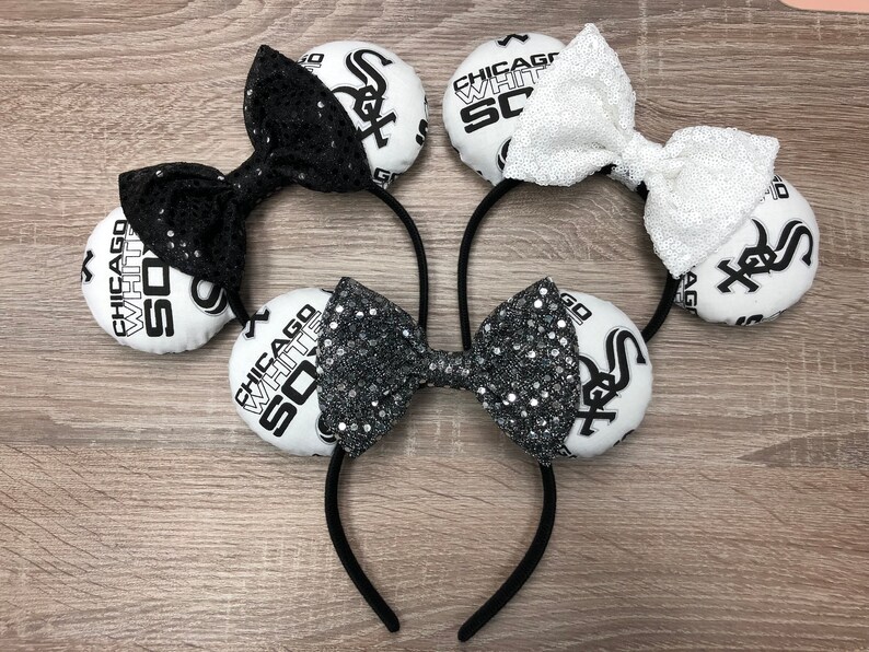 May include: A pair of black and white mouse ears with a black and white bow. The ears are decorated with the words "Chicago White Sox" and the team logo.