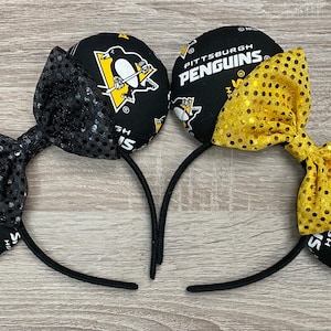 May include: Black and gold Pittsburgh Penguins themed Minnie Mouse ears with a black and gold sequined bow.