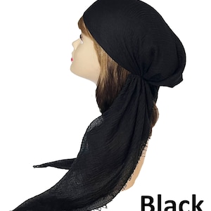 Op de afbeelding: Een effen zwarte hoofddoek met een gekreukte, getextureerde stofafwerking. De hoofddoek is aan de zijkant geknoopt en heeft lange, vloeiende uiteinden met gerafelde randen die naar beneden vallen. Het woord Black staat onderaan in vetgedrukt.