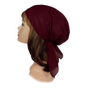 May include: A deep burgundy head scarf tied at the back with two triangular fabric ends. The head covering features a smooth, solid-coloured fabric construction that fits snugly around the crown, providing full coverage with a simple knot design.
