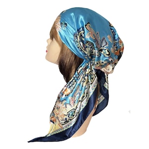 May include: A square satin headscarf in bright blue featuring a multi-colored floral and paisley pattern with a dark navy blue border. The fabric has a smooth, reflective sheen and is tied in a triangular shape, draping down the side of the head.