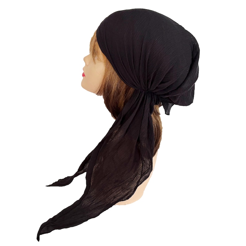 Puede incluir: Un pa&ntilde;uelo negro anudado en la parte trasera, con largas colas sueltas. El cubrecabezas est&aacute; hecho de una tela ligera y texturizada. El pa&ntilde;uelo est&aacute; drapeado sobre una cabeza de maniqu&iacute; con cabello casta&ntilde;o claro y tez clara.