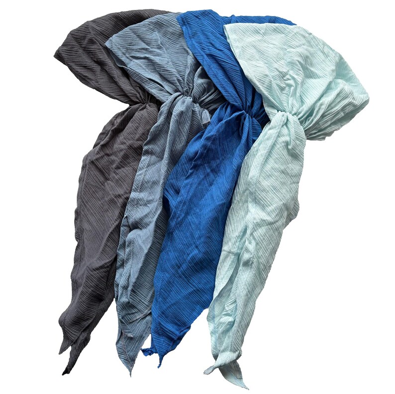 Puede incluir: Cinco pa&ntilde;uelos para la cabeza en tonos azules y grises se muestran sobre un fondo blanco. Los pa&ntilde;uelos est&aacute;n hechos de una tela texturizada y est&aacute;n anudados en la parte superior. Los colores van del gris oscuro al azul claro.