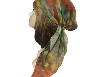 Op de afbeelding: Een hoofddoek met een abstract patroon in tinten oranje, geel, groen en donkerbruin. De lichtgewicht stof is aan de achterkant van het hoofd geknoopt, met een lange, puntige staart die naar beneden valt voor een zacht, gedrapeerd silhouet.
