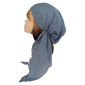 Puede incluir: Un pa&ntilde;uelo para la cabeza azul polvoriento con una tela texturizada y arrugada. El pa&ntilde;uelo se ata en la parte posterior, con extremos de tela largos y fluidos. El pa&ntilde;uelo se muestra en una cabeza de maniqu&iacute; con cabello casta&ntilde;o.