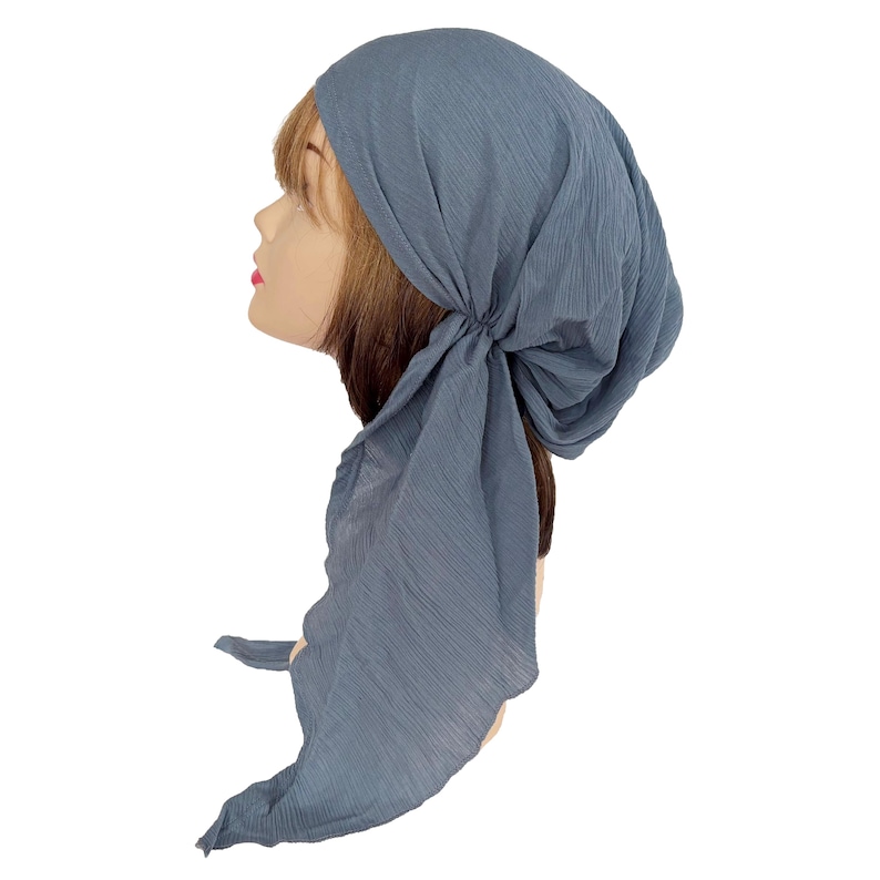 Puede incluir: Un pa&ntilde;uelo para la cabeza azul polvoriento con una tela texturizada y arrugada. El pa&ntilde;uelo se ata en la parte posterior, con extremos de tela largos y fluidos. El pa&ntilde;uelo se muestra en una cabeza de maniqu&iacute; con cabello casta&ntilde;o.