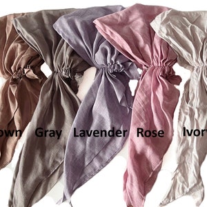 Puede incluir: Cinco cuadrados de tela en diferentes colores: marr&oacute;n, gris, lavanda, rosa y marfil. Los cuadrados est&aacute;n atados en la parte superior y cuelgan.