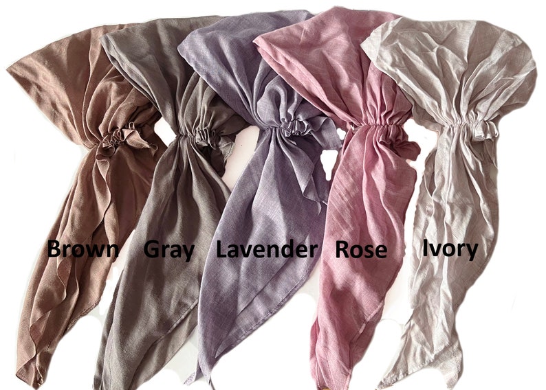 Puede incluir: Cinco cuadrados de tela en diferentes colores: marr&oacute;n, gris, lavanda, rosa y marfil. Los cuadrados est&aacute;n atados en la parte superior y cuelgan.