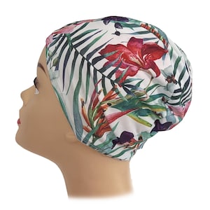 May include: A white cap with a vibrant floral pattern featuring red, purple, and green tropical flowers and leaves. The cap is designed to fit snugly and is likely made of a soft, breathable fabric.