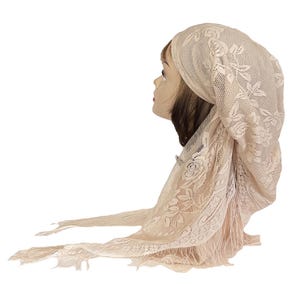 May include: A cream-colored lace head covering with floral patterns. The head covering is draped over a mannequin head, showcasing its delicate design and texture. The lace extends down the sides, with fringed edges.